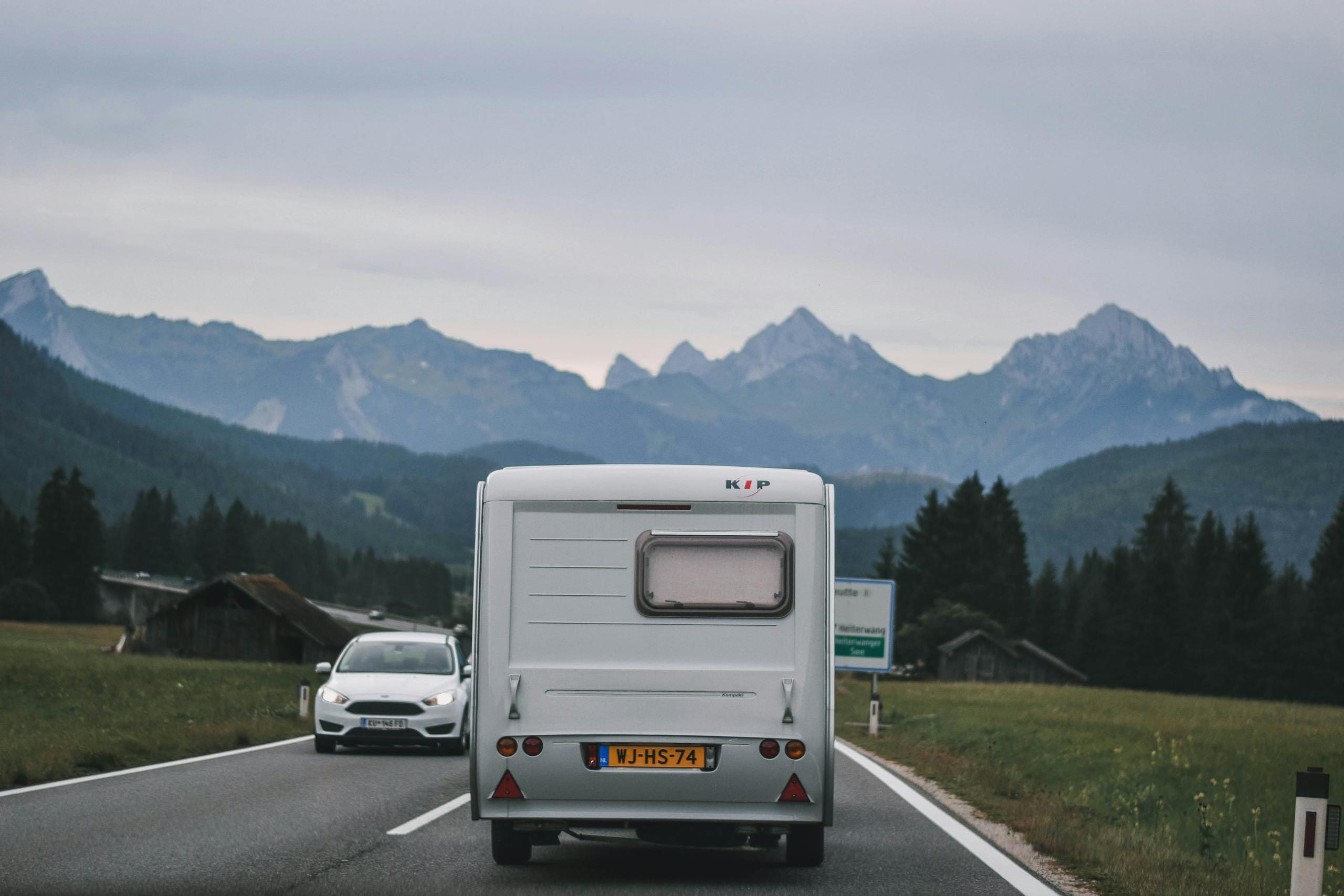 Traveling down a mountain road with caravan and car in scenic countryside.